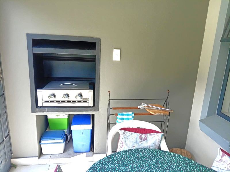 Covered patio area featuring a built-in braai unit and tiled flooring, suitable for outdoor dining and entertainment.