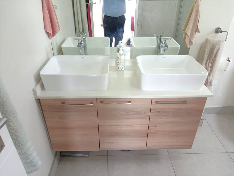 Modern bathroom vanity featuring a double vessel sink setup with stone countertop and wood-finish cabinetry, complemented by a large wall-mounted mirror.
