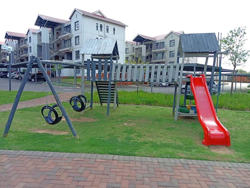 A communal garden area featuring a children's playground set, paved pathways, and well-maintained lawn space within an apartment complex.