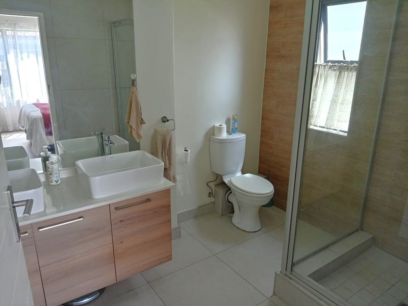 Modern bathroom featuring a wood-finish vanity with vessel sink, a separate shower enclosure, and neutral wall and floor tiling.