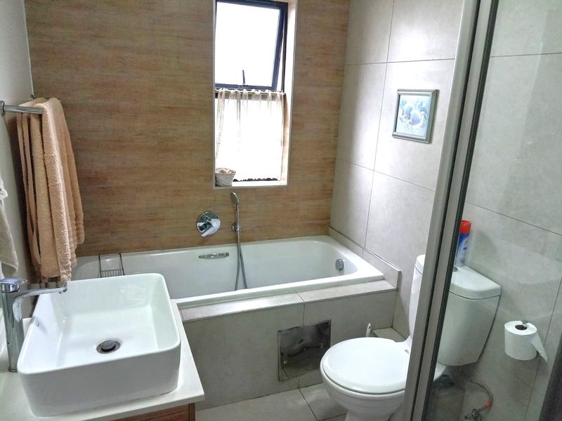 A functional bathroom featuring a built-in bathtub with handheld shower mixer, a modern vessel sink, and a standard toilet with tiled finishes.