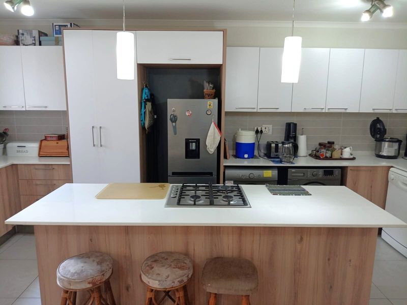 Modern kitchen featuring a central island with a gas cooktop, ample white and wood-tone cabinetry, tiled backsplash, and integrated appliances.
