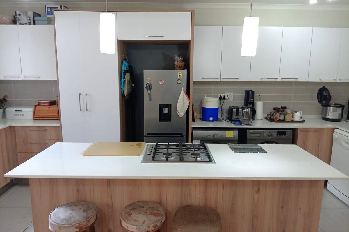 Modern kitchen featuring a central island with a gas cooktop, ample white and wood-tone cabinetry, tiled backsplash, and integrated appliances.