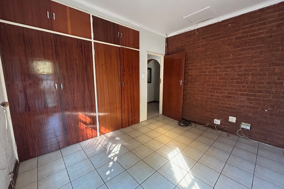 An empty bedroom featuring tiled flooring, a prominent exposed brick wall, and extensive built-in wooden cabinetry.