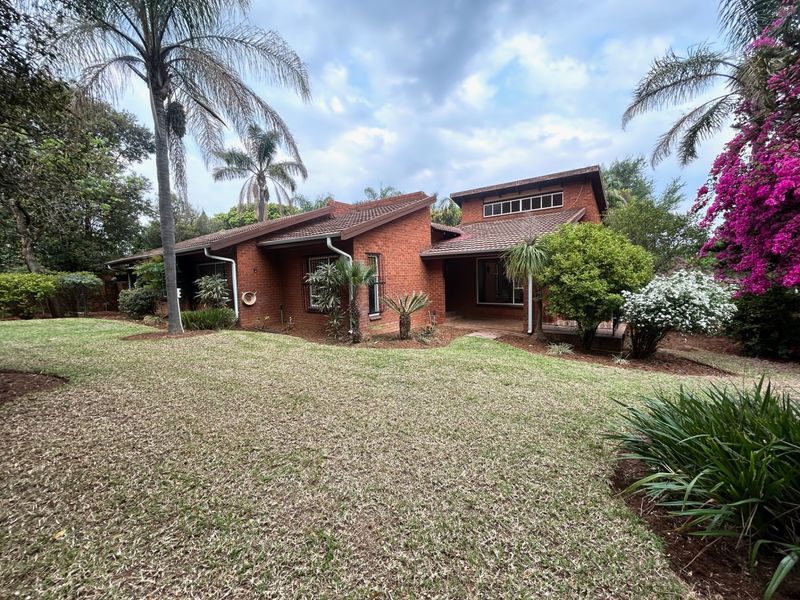 A view of the rear elevation of a brick house featuring a tiled roof, security bars on windows, and a well-maintained garden.