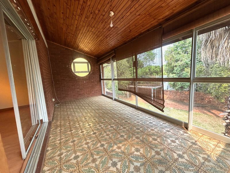 Enclosed patio featuring exposed brick walls, a timber-clad ceiling, patterned floor tiles, and large windows overlooking the garden.