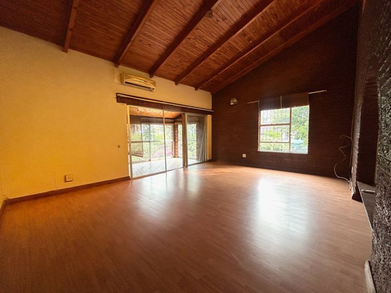 Spacious living area featuring high exposed timber rafter ceilings, laminate flooring, a brick feature wall, and sliding doors leading to an outdoor patio.