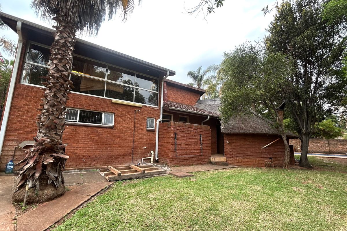 Rear view of a multi-level brick house featuring a thatched roof section, large windows, and an attached patio area requiring maintenance.