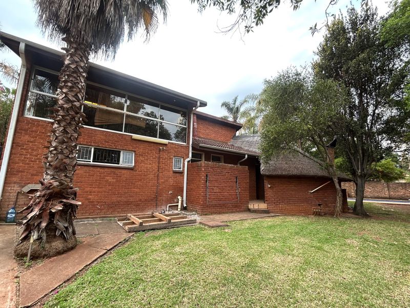 Rear view of a multi-level brick house featuring a thatched roof section, large windows, and an attached patio area requiring maintenance.