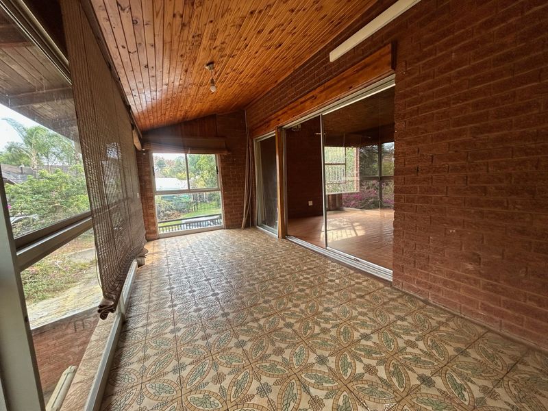 A spacious enclosed patio featuring exposed brick walls, a timber ceiling, and patterned floor tiles, offering a bright transition space to the garden.