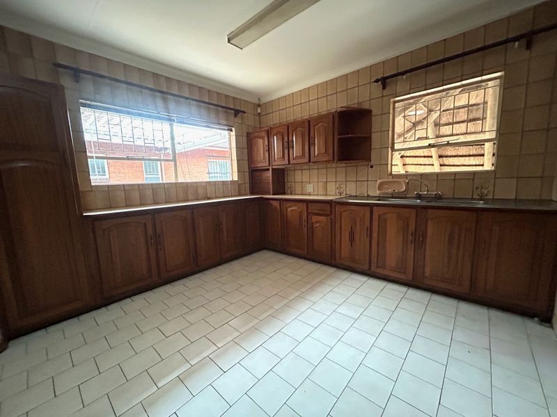 A spacious, dated kitchen featuring extensive wooden cabinetry, tiled walls, and tiled flooring, offering a blank canvas for a modern renovation.