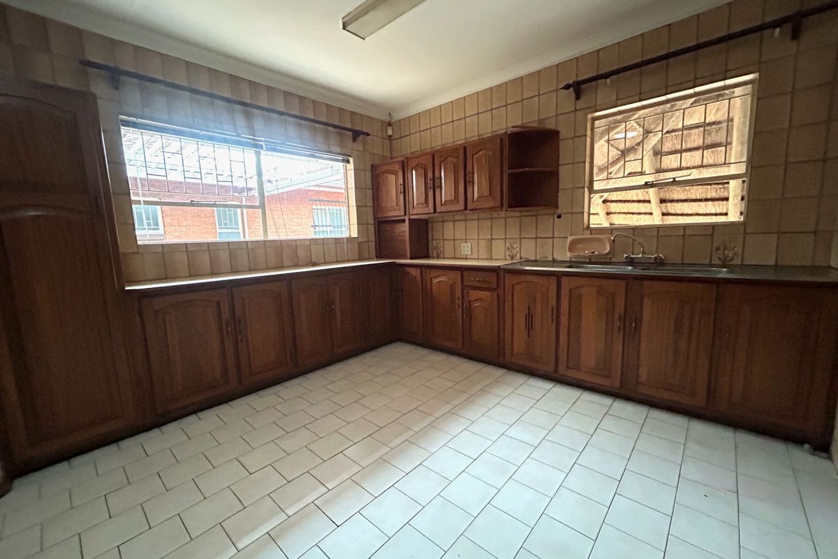 A spacious, dated kitchen featuring extensive wooden cabinetry, tiled walls, and tiled flooring, offering a blank canvas for a modern renovation.