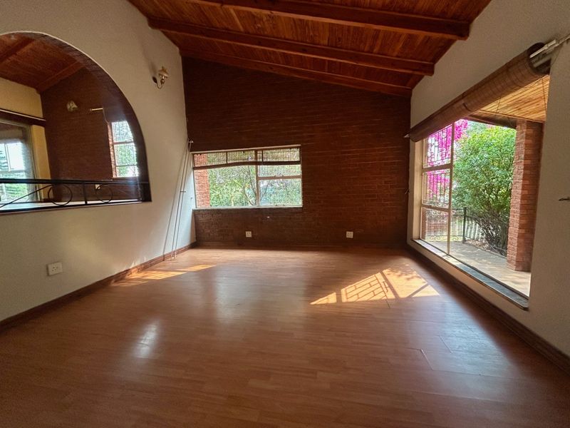Spacious living area featuring exposed timber beam ceilings, a rustic brick feature wall, and large windows providing natural light and garden views.