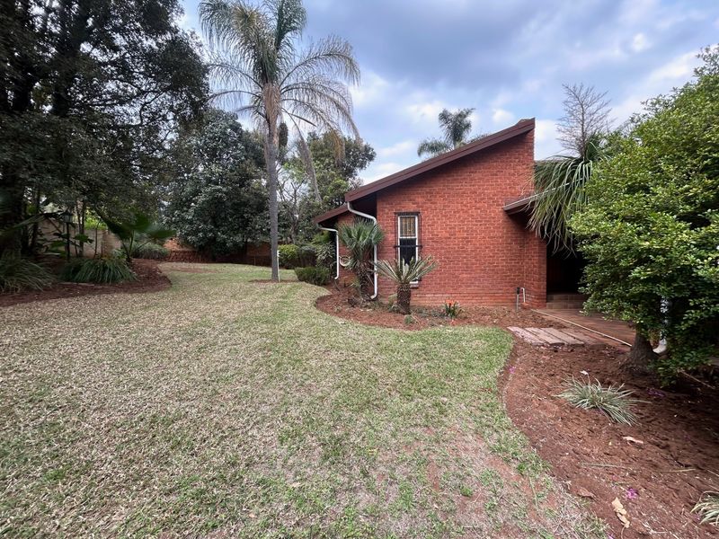 A view of the rear brick facade of the house, featuring a well-maintained garden with mature trees and established landscaping.