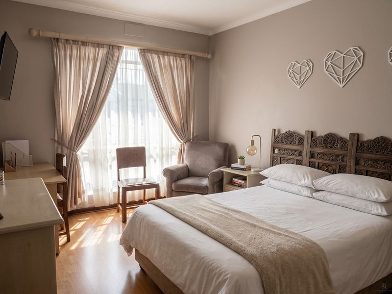 A well-lit bedroom featuring laminate flooring, neutral wall tones, and a large window with curtain fixtures, creating a comfortable and inviting living space.