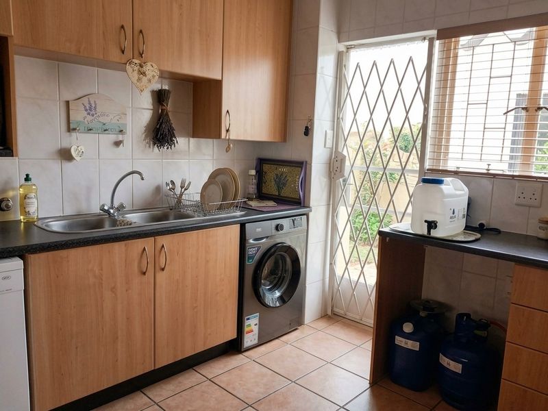 Functional kitchen featuring laminate cabinetry, tiled backsplash, stainless steel sink, and direct access to the exterior via a security gate.
