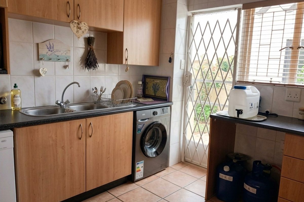 Functional kitchen featuring laminate cabinetry, tiled backsplash, stainless steel sink, and direct access to the exterior via a security gate.