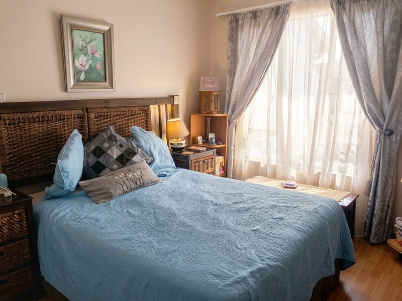 A cozy bedroom featuring laminate flooring and natural light through a window with installed curtain tracks.