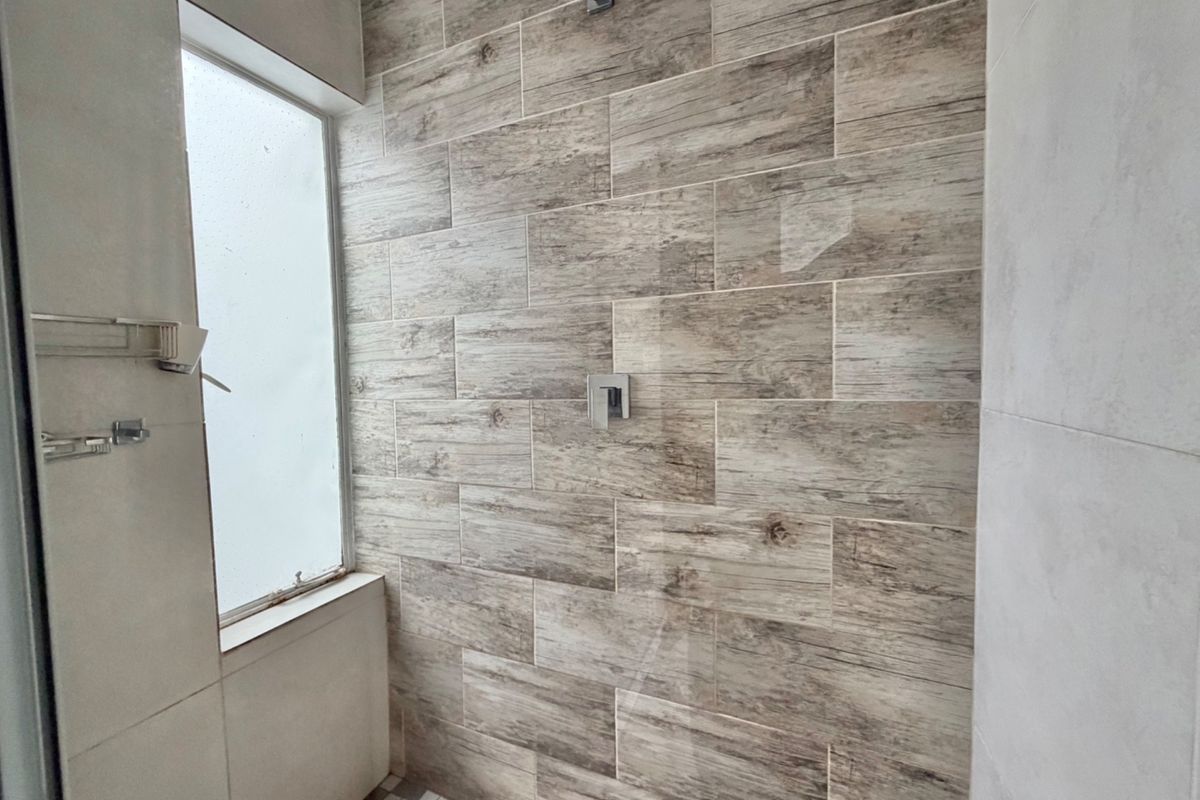 Modern walk-in shower featuring wood-look ceramic wall tiles, mosaic floor tiling, and a frosted glass window for natural light.