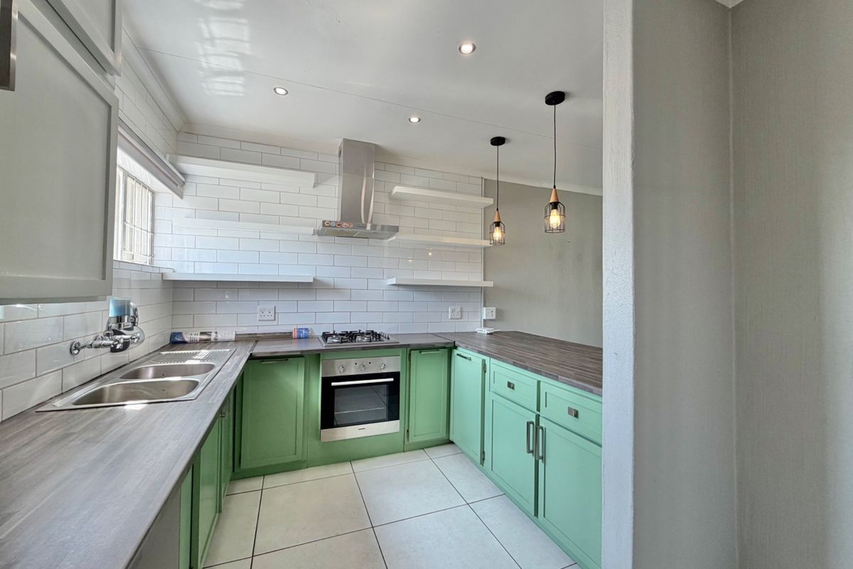 A modern, well-lit kitchen featuring green cabinetry, dark laminate countertops, subway tile backsplash, and integrated stainless steel appliances.