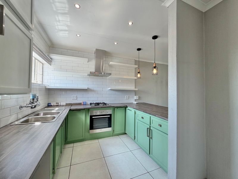 A modern, well-lit kitchen featuring green cabinetry, dark laminate countertops, subway tile backsplash, and integrated stainless steel appliances.