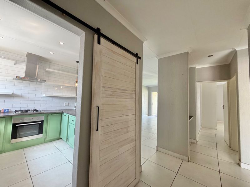 Open plan living area featuring a modern kitchen with green cabinetry, gas hob, and a stylish sliding barn door leading to the hallway.