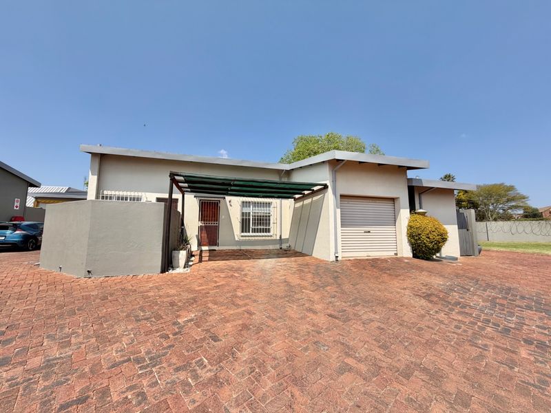 Front elevation of a townhouse featuring a paved driveway, single garage, and a covered carport area with security features.