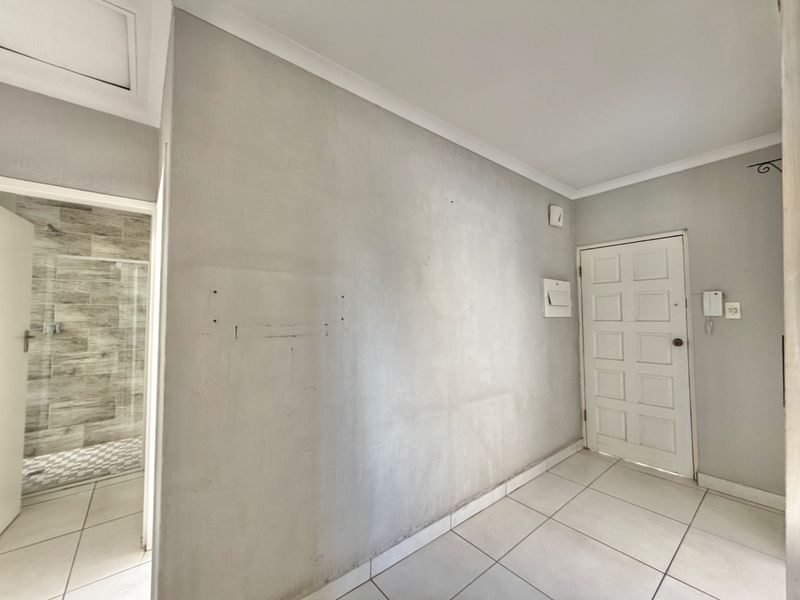 A vacant hallway featuring tiled flooring, coved ceilings, and access to an adjacent bathroom, with visible wall imperfections requiring minor cosmetic attention.