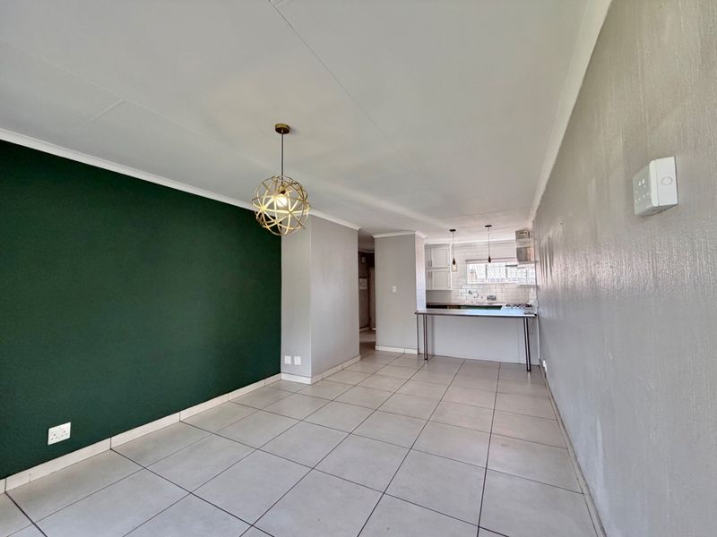 An open-plan living and kitchen area featuring neutral tiled flooring, a dark green accent wall, and a functional kitchen with built-in cabinetry.
