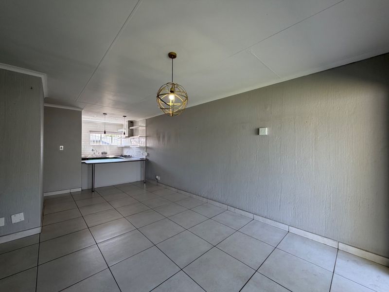 An open-plan living and kitchen area featuring neutral tiled flooring, a breakfast counter, and functional kitchen cabinetry with integrated appliances.