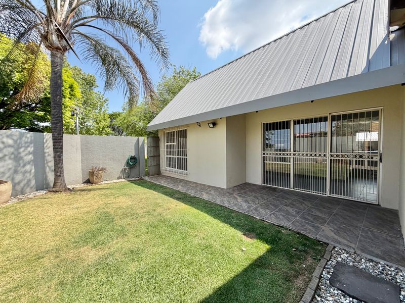 Rear view of the townhouse featuring a tiled patio, secure sliding doors, and a private garden area with a perimeter wall.