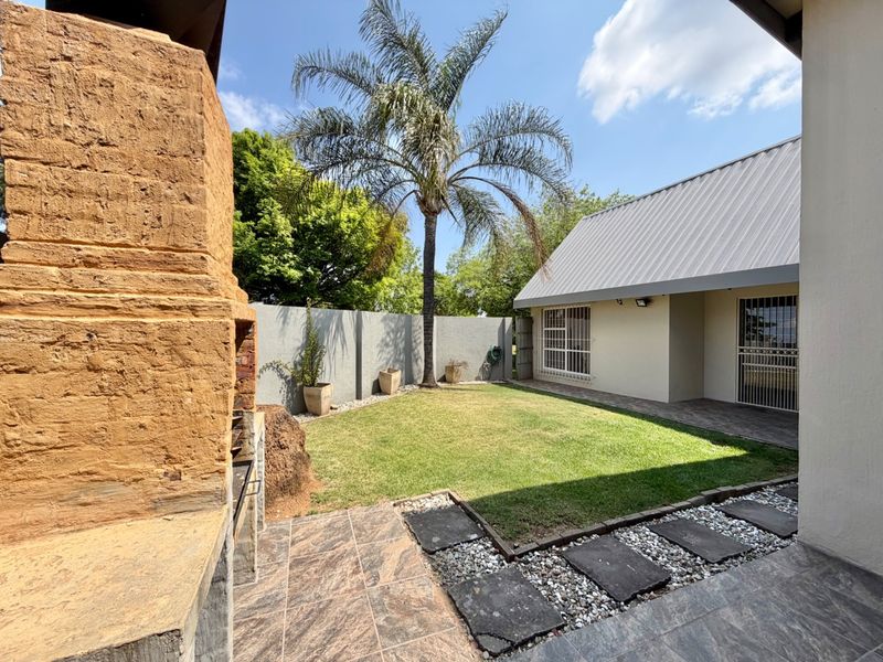 A private rear garden featuring a tiled patio, built-in braai, and a well-maintained lawn enclosed by boundary walls.