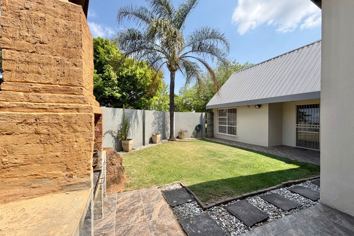 A private rear garden featuring a tiled patio, built-in braai, and a well-maintained lawn enclosed by boundary walls.