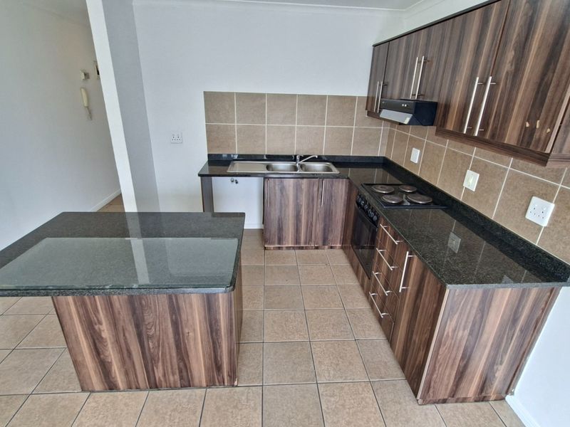 A clean, functional kitchen featuring wood-finish cabinetry, granite countertops, a built-in oven and hob, and a convenient central island.
