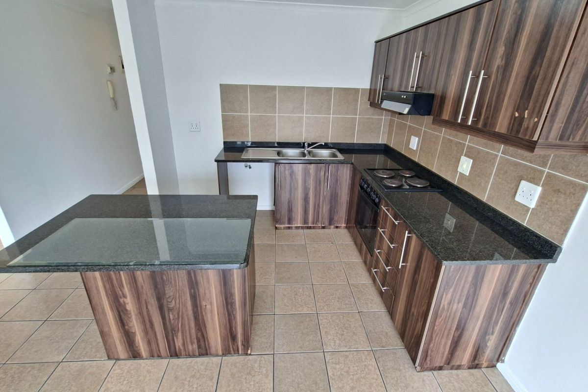 A clean, functional kitchen featuring wood-finish cabinetry, granite countertops, a built-in oven and hob, and a convenient central island.