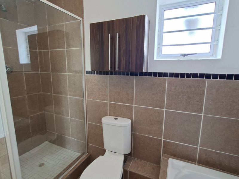 A functional bathroom featuring a glass shower enclosure, wall-mounted storage cabinet, and neutral ceramic tiling throughout.