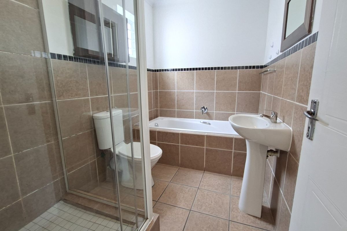 A functional bathroom featuring a pedestal basin, toilet, bathtub, and a separate glass-enclosed shower with neutral wall and floor tiling.