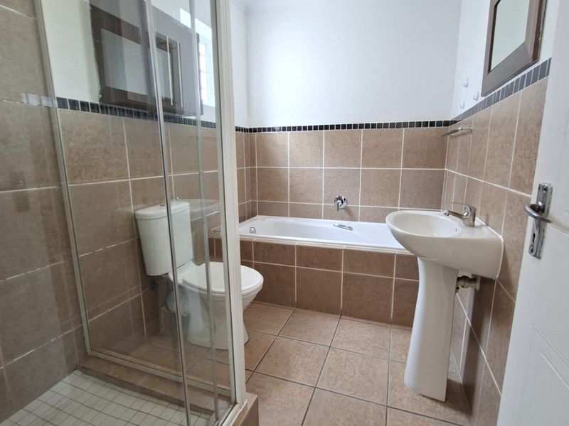 A functional bathroom featuring a pedestal basin, toilet, bathtub, and a separate glass-enclosed shower with neutral wall and floor tiling.