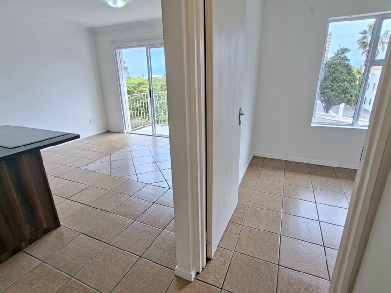 An open-plan living area featuring tiled flooring, a kitchen island, and a sliding door leading to a balcony with exterior views.