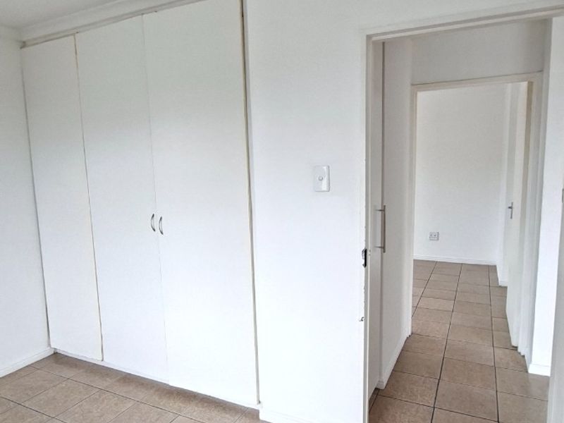 A clean, empty bedroom featuring neutral tiled flooring, built-in cupboards, and coved cornicing, leading into a connecting hallway.