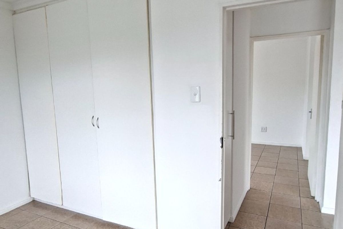 A clean, empty bedroom featuring neutral tiled flooring, built-in cupboards, and coved cornicing, leading into a connecting hallway.