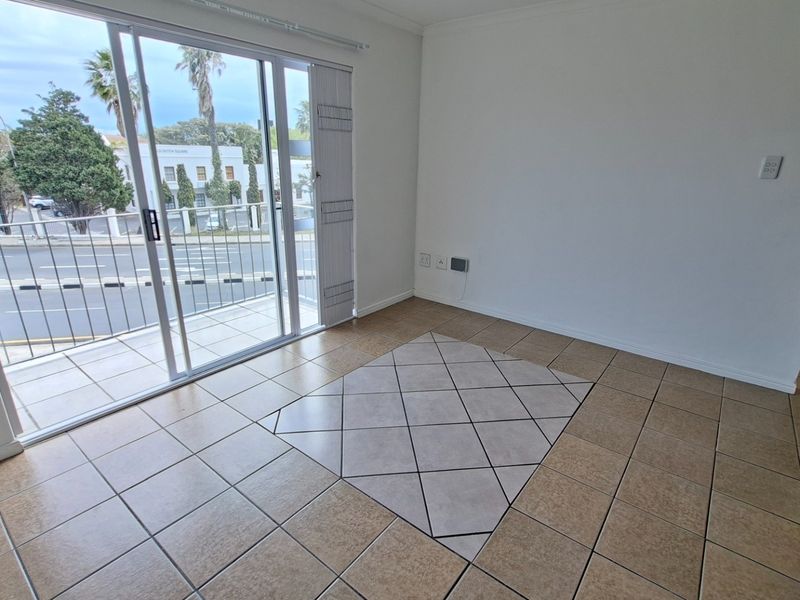 An empty living area featuring tiled flooring, a decorative tile inlay, and large sliding glass doors providing access to a balcony.