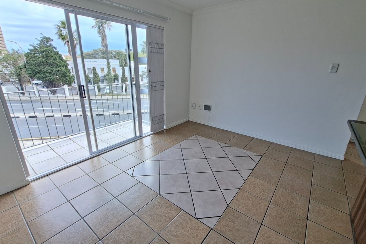 An empty living area featuring tiled flooring, a decorative tile inlay, and large sliding glass doors providing access to a balcony.
