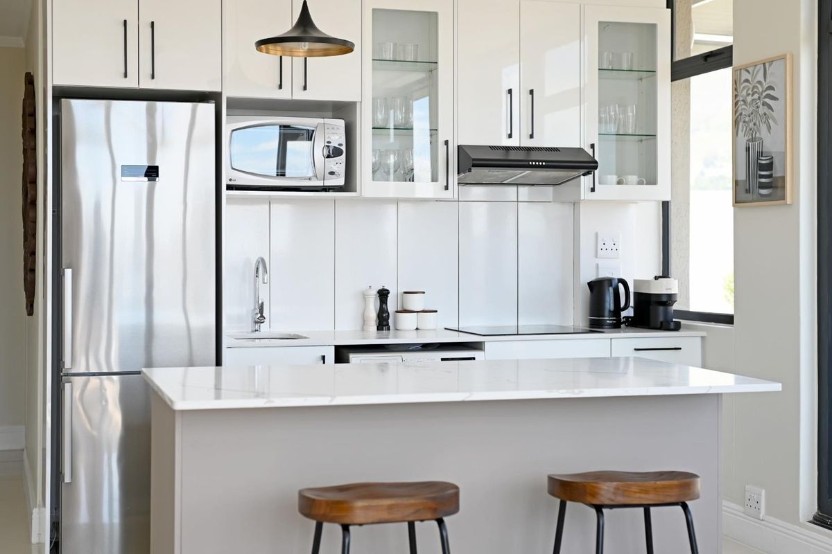 Modern kitchen featuring white gloss cabinetry, stone countertops, a central island, and integrated appliances, offering a clean and contemporary aesthetic.