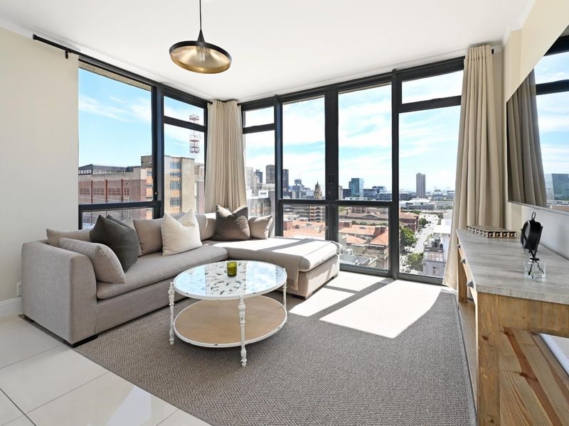 Bright and modern living room featuring expansive floor-to-ceiling windows with panoramic city views and sleek tiled flooring.