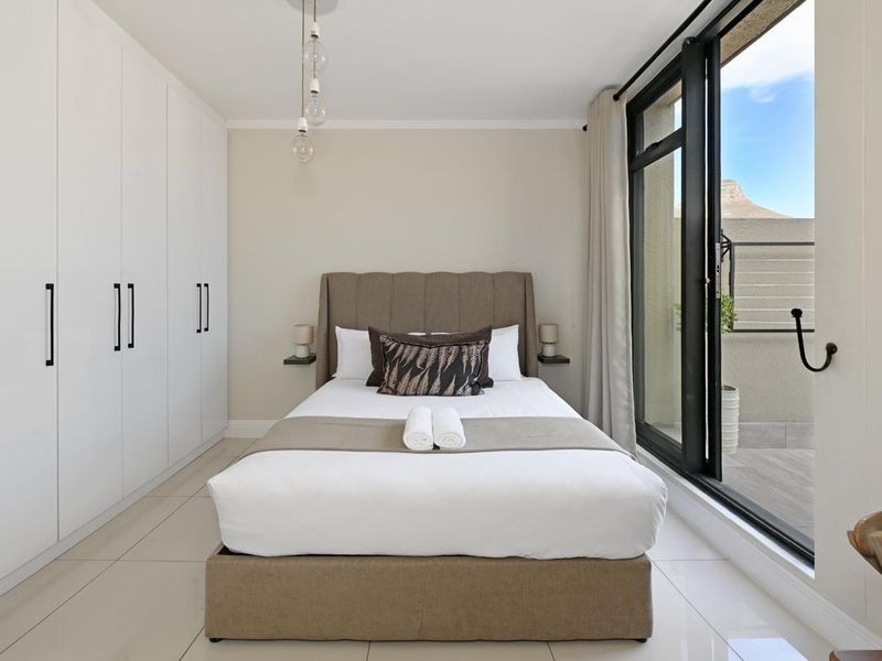 A modern bedroom featuring built-in cupboards, sleek tiled flooring, and a large sliding glass door providing access to a private balcony.