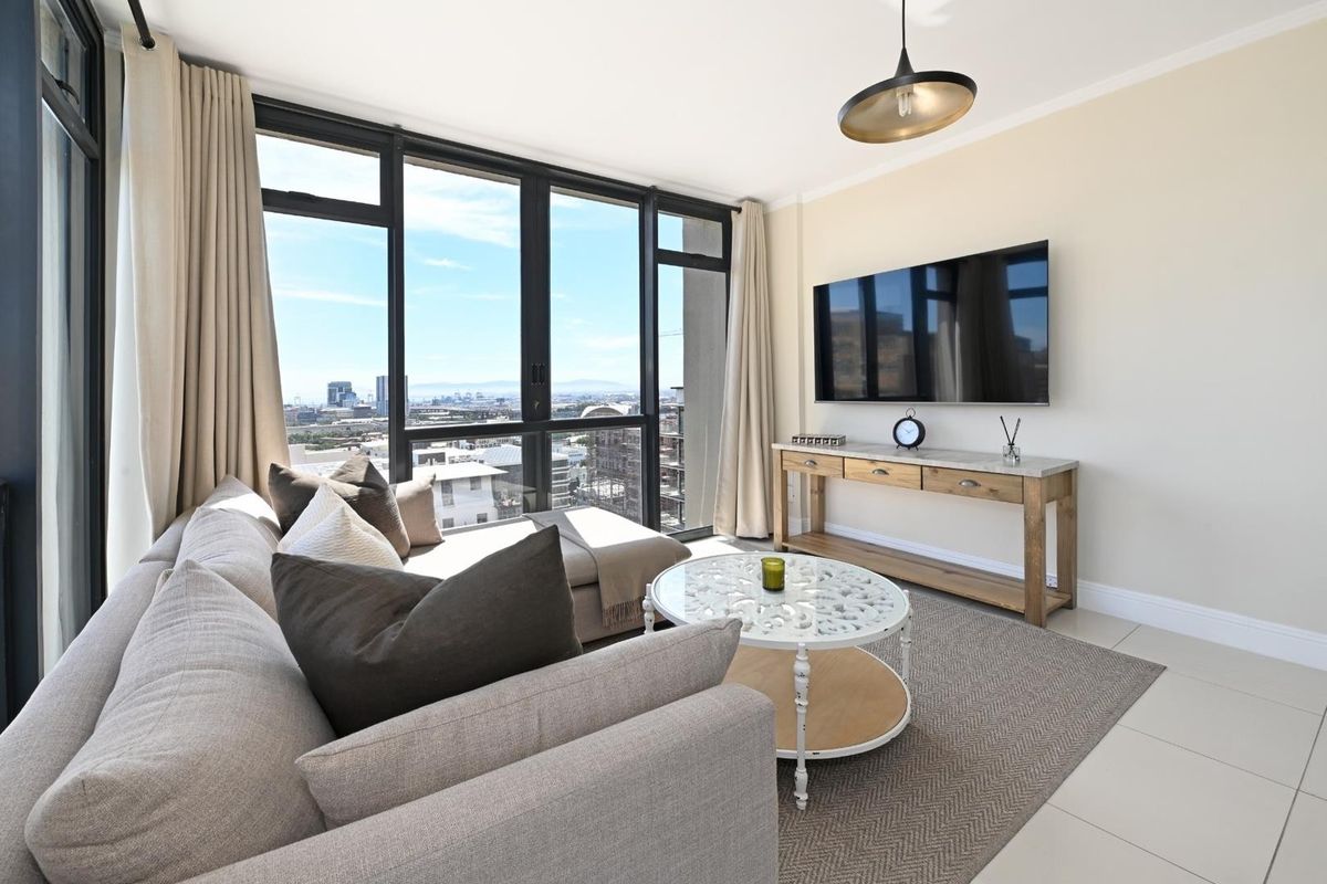 A bright living room featuring floor-to-ceiling windows with expansive city views, neutral tiled flooring, and modern pendant lighting.