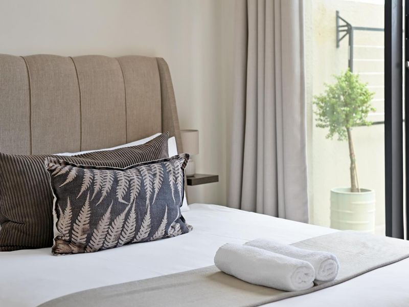 A well-maintained bedroom featuring neutral tones, a modern headboard, and direct access to an outdoor area through a sliding glass door.