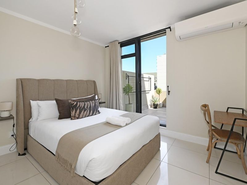 A well-maintained bedroom featuring tiled flooring, a split-system air conditioner, and direct access to a private balcony through a sliding glass door.