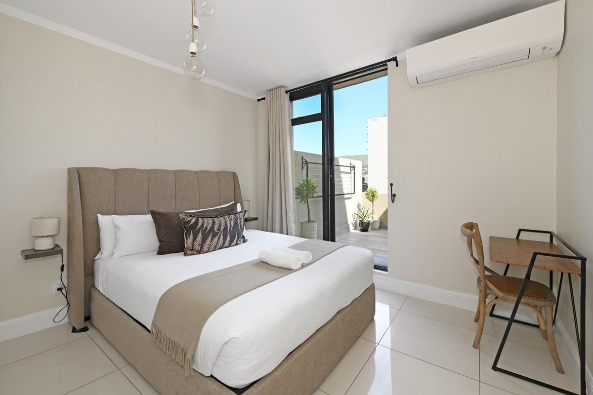 A well-maintained bedroom featuring tiled flooring, a split-system air conditioner, and direct access to a private balcony through a sliding glass door.